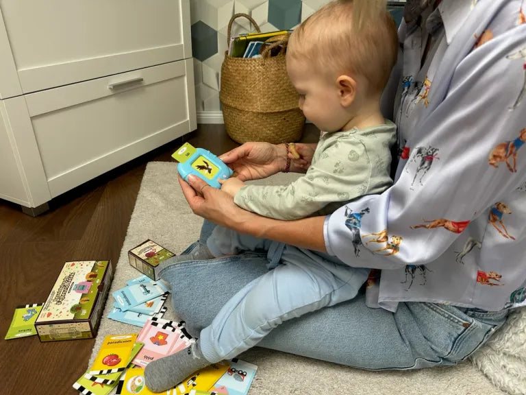 Mamička so synom v lone spoločne používajú modrú Kinderspeech čítačku s edukačnými kartičkami na zemi.